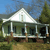 Pixelated static image of a house with a white gabled roof, green walls, and a porch with white columns, set against a blue sky and green foliage.