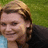 Pixelated image of a person with light brown hair and dark eyes, wearing a black top against a green background.