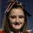 Pixelated image of a person with long brown hair wearing a red and white striped headband, dark eyeliner, and a red top against a dark blue background.