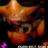 Pixelated orange and brown cartoon character with large eyes and a wide mouth, set against a dark background with a small pink plus sign in the corner.