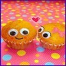 Two cartoon-style muffins with large eyes and smiling faces stand side-by-side on a polka-dotted background, with a small red heart floating above them.