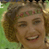 Static pixelated image of a person with curly brown hair wearing a green headband with pink flowers, smiling broadly against a blurred outdoor background.