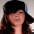 A static pixelated image of a person with long brown hair wearing a black cap, closed eyes, and a neutral expression against a light background.
