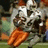 A pixelated image of a football player in a silver uniform with orange pants, holding a football, with green text overlays changing across frames.