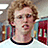 A pixelated image of a person with curly light brown hair wearing a white shirt with black collar, set against a blue background with orange text.