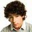 Pixelated image of a person with curly brown hair wearing a gray sweater over a white collared shirt, set against a light pink background with green text.