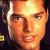 Pixelated close-up of a person's face with warm orange and yellow tones, visible facial features including eyes, nose, mouth, and hair, set against dark background.
