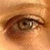 A close-up of a human eye with brown iris and eyelashes, set against warm-toned skin tones in pixelated detail.