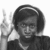 Black-and-white image of a person with short dark hair wearing a headband, making a peace sign with their right hand against a white background.