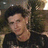 A person with dark curly hair wearing a black shirt appears in three showing slight head and eye movement against an indistinct background