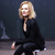 A pixelated figure with blonde hair sits in profile, wearing a black outfit and white shoes against a dark background.