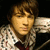 Pixelated static image of a person with light brown hair wearing a patterned shirt and dark tie, leaning against a metallic object.