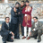 Group of people in formal attire with one person in red dress standing center, others seated or standing around; red text 'done' on black background.