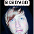A pixelated image of a person with light brown hair and blue eyes, wearing a dark hooded garment against a black background.