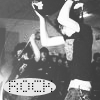 Black-and-white image of a person in dark clothing holding a microphone, with a crowd in the background and a pixelated oval text box at the bottom.