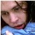 Pixelated close-up of a person's face with closed eyes, dark hair, and a blue garment visible below the chin.
