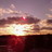 Pixelated sunset scene with gradient sky transitioning from purple to orange, reflecting on dark water below.