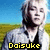 Pixelated image of a person with light hair and beard wearing dark clothing, standing against blue sky and green field background with yellow text at bottom.