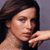Pixelated close-up of a person with dark hair resting their chin on a hand against a gray background.