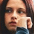 A pixelated close-up of a person with dark hair, light skin tone, and brown eyes wearing a white shirt over blue clothing.