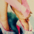 Pixelated image of two figures in close embrace, one with light hair and pink tones, the other with dark teal clothing.