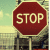 A red octagonal stop sign with white text reading 'STOP' on a pole, set against a blurred background of light blue sky and yellowish ground.