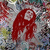 A red, stylized figure with flowing hair and a circular white face against a pixelated background of muted colors.