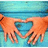 Two hands form a heart shape against a blue wooden background, with one hand wearing a black bracelet.