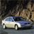 Pixelated image of a light-colored sedan with dark windows and blue accents, positioned on a road against a blurred background.