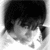 Pixelated grayscale image of a figure with dark hair and light clothing against a white background, showing partial facial features and body shape.