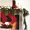 A fireplace mantel adorned with green garland, two red stockings, white flowers, and red poinsettias, with a lit fire below.