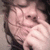 A person with dark hair and light skin covers their mouth with a hand, showing a slight smile in a static image.