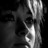 Black-and-white close-up of a person's face with visible hair strands, eyes, nose, and mouth against a dark background.
