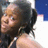 Pixelated close-up of a person with dark hair and light skin, wearing a sleeveless top against a blue background.