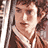 Static 48x48 pixel buddy icon depicting a close-up of a person with brown hair and light skin tone, wearing a dark top with white collar detail, set against a blurred background.