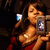 Woman in red dress holding camera with blue and white screen, dark background, pixelated style.