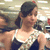 A pixelated image of a person with dark hair tied back, wearing a white and dark blue sleeveless top, against a blurred background with light and dark tones.