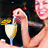A woman in a black dress holds a stemmed glass with light yellow liquid and green garnish, smiling while stirring the drink.