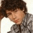 A pixelated image of a person with dark curly hair wearing a gray patterned shirt, shown in two states: one without text and one with pink text overlay.