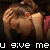 Pixelated image of a person with light brown hair covering their face with both hands, wearing a dark top with red accents, and white text reading "u give me headache" at the bottom.