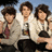 Three people in white jackets sit together on a pink background with yellow text reading "The Jonas Brothers," "Love," and "Abbey Marie Davis <3."