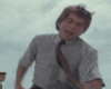 A man in a light gray striped shirt and brown tie performs dynamic movements against a cloudy sky background.