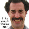 Static image of a man with dark curly hair and a thick mustache, wearing a gray shirt against a white background, with text overlay on the left side.
