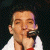 A pixelated image showing a person holding a microphone on the left and green text reading "Original Icons .com" on the right against a dark background.