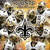 A static icon featuring a symmetrical pattern of stylized skulls with black fleur-de-lis symbols on their foreheads, set against an orange and white background.