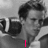 A black-and-white photo of a person with curly hair holding a camera, overlaid with pink text that changes across four