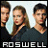 Three people in dark clothing stand side-by-side against a light background with the word ROSWELL below them.
