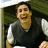 Pixelated image of a person in a dark vest over a light shirt, smiling with mouth open, against a greenish background with white elements.