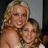 Two people with light brown hair pose closely together, one behind the other, against a neutral gray background.