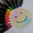 Pixelated cartoon face with a smiling expression, wearing a colorful striped scarf and green hair accessory against a light background.